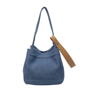 Blue denim tote bag with brown leather strap detail shown on a white background