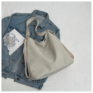 Detail of light gray canvas tote bag with wide strap and silver metal hardware accents