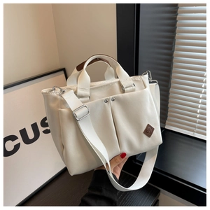 Detail of cream canvas tote bag featuring front pockets and brown leather handle wrap