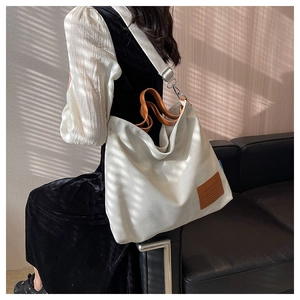 Detail of canvas tote bag showing brown leather logo and textured fabric under natural light