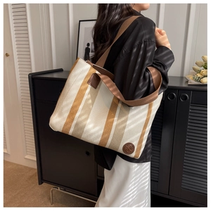 Detail of a large striped canvas tote bag featuring brown leather logo and wide woven straps