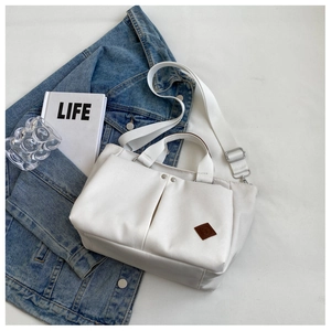 Macro view of white canvas tote bag detail featuring large pockets and adjustable strap