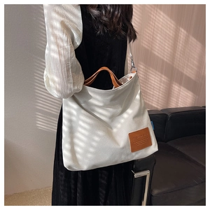 Detail of white canvas tote bag featuring brown leather strap and logo patch decoration