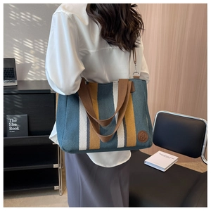 Detail view of large striped canvas tote bag with brown woven strap for daily commuting
