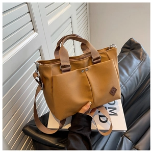 Detail of camel tote bag featuring dual front metal buckle pockets and wide strap