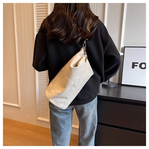 Detail of a large cream canvas crossbody bag with brown leather accents and metal hooks