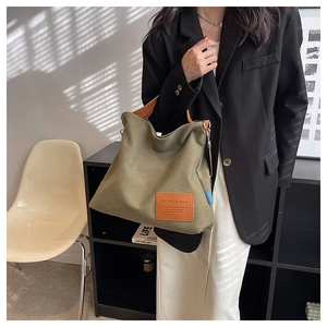 Detail of olive green canvas tote bag featuring brown leather strap and brand patch