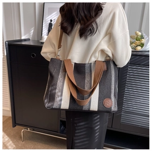 Detailed back view of a large striped canvas tote bag worn by a model in a home setting