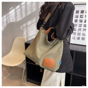 Detail view of large olive green canvas tote bag with brown leather handles and brand tag