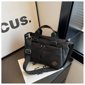 Detail of black canvas tote bag showing silver rivets and brown leather strap accents