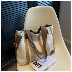Detail of striped canvas tote bag with adjustable strap and circular logo on a chair