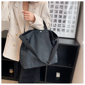 Détail du grand sac cabas en toile noire porté à l'épaule par un mannequin de mode