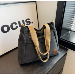 Détail d'un sac cabas en toile montrant le tissu noir et l'écusson en cuir du logo