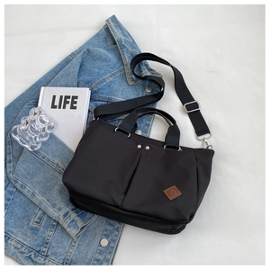 Detail of a black canvas tote bag with front pockets, wide strap, and lifestyle props