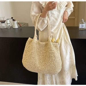 Detail of woven straw tote bag in off-white finish held by model in floral dress