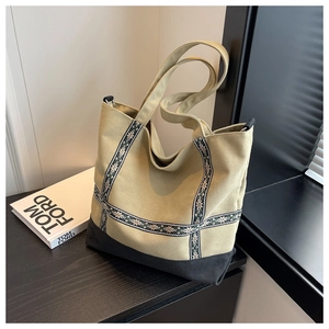 Detail of khaki and black canvas tote bag with ethnic woven straps on a dark surface