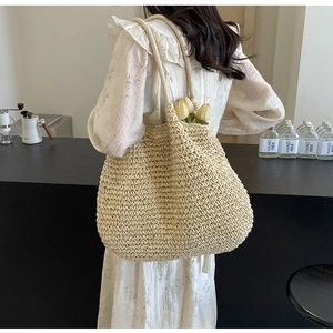 Détail d'un grand sac cabas en paille porté à l'épaule dans un décor de café chic