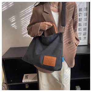 Detail of black canvas tote bag with brown leather handles and rectangular patch