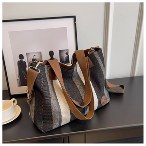 Close-up of striped canvas tote bag with brown handles and a round leather logo detail