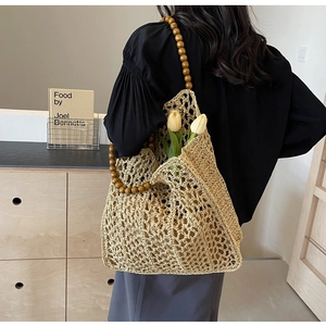 Detail of hand-woven hollow straw tote bag with round brown wooden bead handles