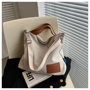 Detail of off-white canvas tote bag with brown leather handles and adjustable strap