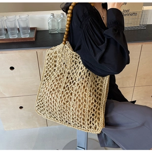 Detail of woven straw tote bag with retro dark brown wooden bead handle on model