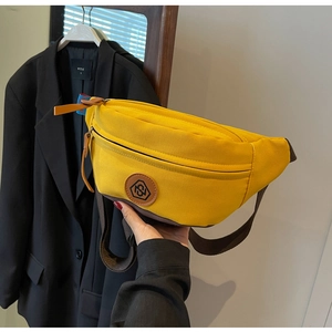Detail view of bright yellow canvas crossbody bag with adjustable brown strap and logo