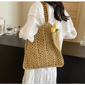 Detail of woven straw tote bag featuring brown wooden bead handles and hollow mesh pattern