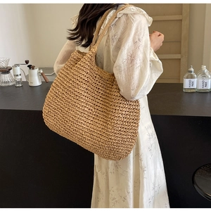 Vue détaillée d'un grand sac à bandoulière en paille tressée porté par un mannequin au café