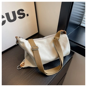 Detailed close-up of cream canvas crossbody bag with contrast brown strap and metal buckle