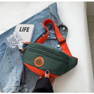 Detail of dark green canvas crossbody bag with orange strap and round leather logo patch