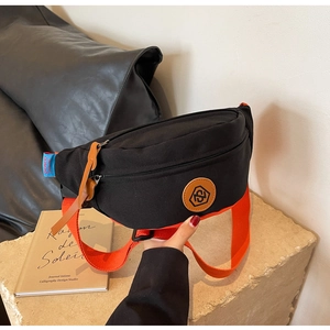 Detail of black canvas crossbody bag featuring a vibrant orange wide woven shoulder strap
