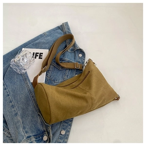 Detail of mustard brown canvas crossbody bag with wide strap and zip on denim jacket