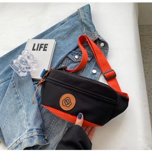 Detail of canvas crossbody bag showing black and orange contrast and round logo patch