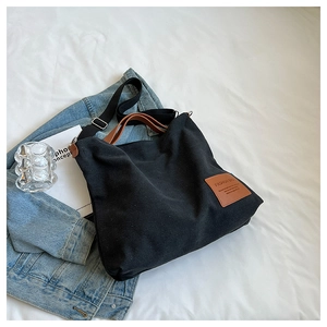 Close-up of black canvas tote bag with brown leather handles and brand label on white fabric