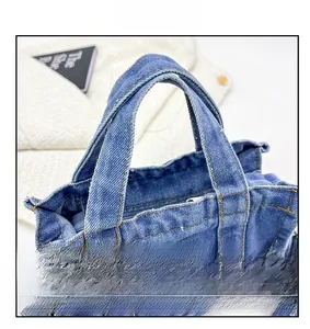 Detailed close-up of blue denim tote bag with yellow stitching and metal buckle