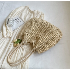 Vue à plat d'un sac cabas en paille tressée beige sur tissu blanc avec accessoires lifestyle