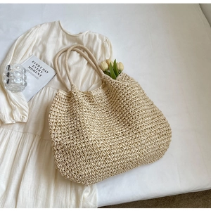 Vista piatta di borsa in paglia intrecciata beige su un abito con tulipani per stile estivo