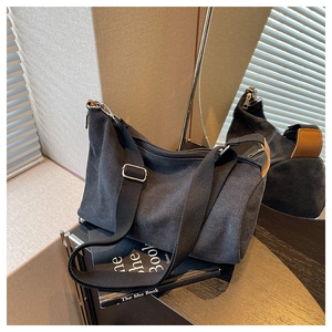 Detail of black canvas crossbody bag featuring adjustable wide strap and silver metal hardware