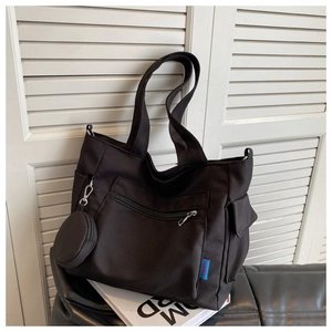 Detail of black Oxford fabric tote bag showing zipper pockets and small coin purse attachment