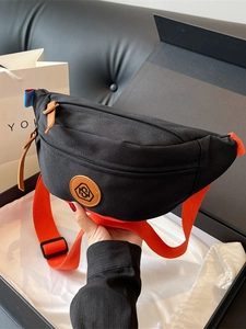 Minimalist black canvas chest bag with adjustable orange strap shown in a gift box
