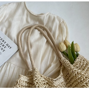 Dettaglio di una grande borsa tote in paglia kaki con tulipani e tessuto crema a pieghe
