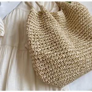 Dettaglio borsa tote in paglia intrecciata a mano con trama fine su sfondo crema