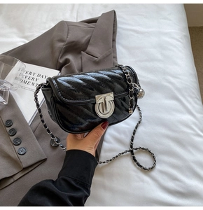 Detail of quilted patent leather crossbody bag with silver chain strap and metal ball charm