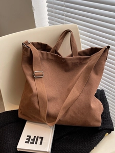 Grand sac cabas en toile marron foncé avec bandoulière réglable sur chaise blanche
