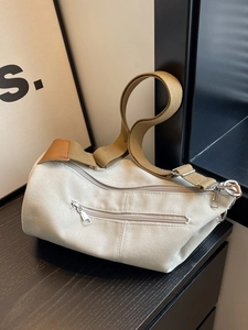 Chic cream canvas barrel bag with brown shoulder strap shown on a wooden table
