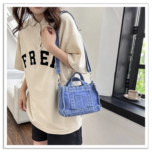 Detail of blue denim mini tote bag with dual handles and adjustable shoulder strap