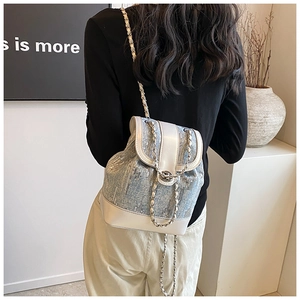 Rear view of a blue sequin bucket backpack with chain straps on a model in a minimal room