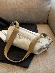 Minimalist canvas cylinder bag with wide brown strap on a dark blazer and sofa