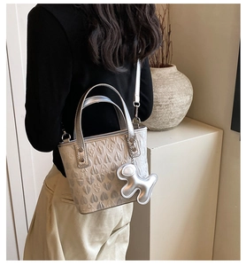 Silver heart-embossed handbag shown on model with metallic dog charm and thin strap